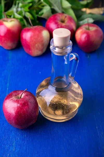 Apfelessig. eine Glasflasche auf blauem Hintergrund. rote Äpfel. — Stockfoto