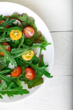 Beyaz ahşap zemin üzerinde Kamkat ve domates kiraz ile taze Roka Salatası. Üstten Görünüm. Sağlıklı gıda. Diyet.