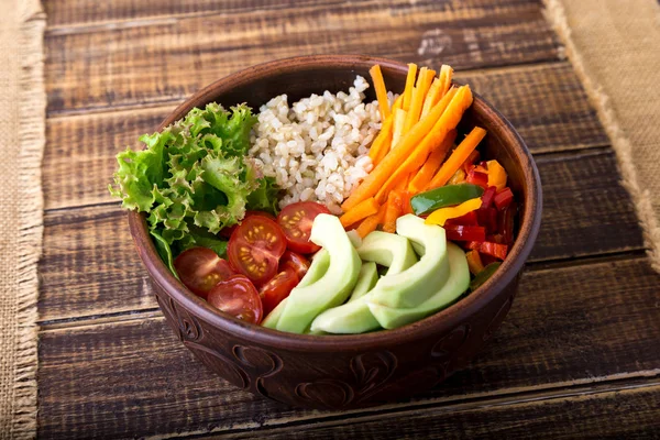 Vegan buddha bowl on wooden background. Bowl with carrot, lettuce, tomatoes cherry, pepper, avocado and porridge. Vegetarian, healthy, detox food concept.