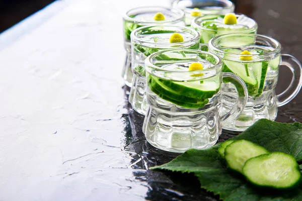 Cucumber water in six little mason glass jar on black background.