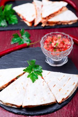 Mexican quesadilla kırmızı ahşap arka plan üzerinde siyah arduvaz taş plaka üzerinde salsa ile. Biber biber.