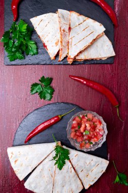 Mexican quesadilla kırmızı ahşap arka plan üzerinde siyah arduvaz taş plaka üzerinde salsa ile. Biber biber. Üstten Görünüm.