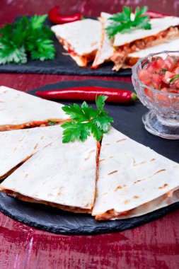 Mexican quesadilla kırmızı ahşap arka plan üzerinde siyah arduvaz taş plaka üzerinde salsa ile. Biber biber.