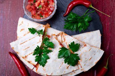 Mexican quesadilla kırmızı ahşap arka plan üzerinde siyah arduvaz taş plaka üzerinde salsa ile. Biber biber. Üstten Görünüm.