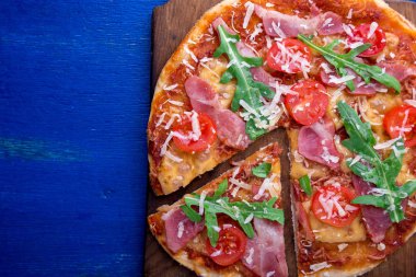 Ev yapımı pizza salam, domates, roka ahşap Pano mavi zemin üzerine. Üstten Görünüm.