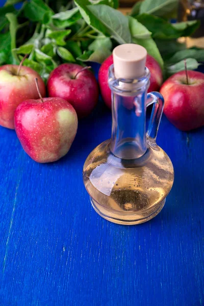 Vinagre de manzana. Una botella de vidrio sobre fondo azul. Manzanas rojas . — Foto de Stock