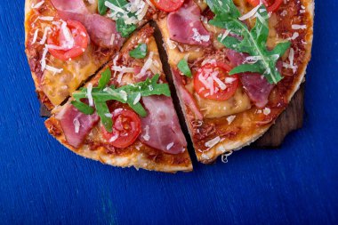 Ev yapımı pizza salam, domates, roka ahşap Pano mavi zemin üzerine. Üstten Görünüm.