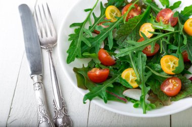 Beyaz ahşap zemin üzerinde Kamkat ve domates kiraz ile taze Roka Salatası. Üstten Görünüm. Sağlıklı gıda. Diyet.