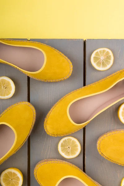 Sepatu espadrilles kuning dekat irisan lemon di latar belakang kayu. Tampilan atas. — Stok Foto