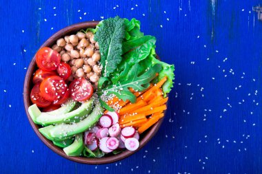 Vegan Buda kase mavi ahşap zemin üzerinde. Havuç, marul, kiraz domates, turp, avokado ve Nohut ile top. Vejetaryen, sağlıklı, detoks gıda kavramı. Üstten Görünüm.
