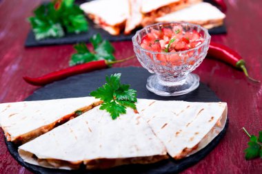 Mexican quesadilla kırmızı ahşap arka plan üzerinde siyah arduvaz taş plaka üzerinde salsa ile. Biber biber.