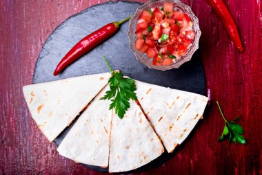 Mexican quesadilla kırmızı ahşap arka plan üzerinde siyah arduvaz taş plaka üzerinde salsa ile. Biber biber. Üstten Görünüm.