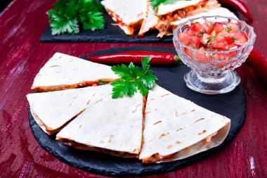 Mexican quesadilla kırmızı ahşap arka plan üzerinde siyah arduvaz taş plaka üzerinde salsa ile. Biber biber.