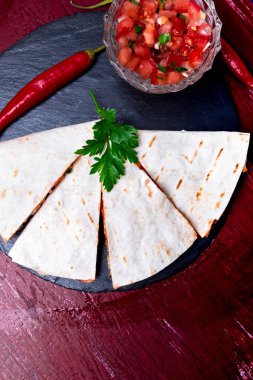 Mexican quesadilla kırmızı ahşap arka plan üzerinde siyah arduvaz taş plaka üzerinde salsa ile. Biber biber. Üstten Görünüm.