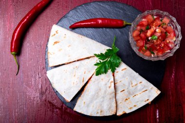Mexican quesadilla kırmızı ahşap arka plan üzerinde siyah arduvaz taş plaka üzerinde salsa ile. Biber biber. Üstten Görünüm.