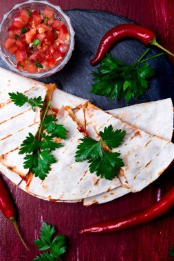 Mexican quesadilla kırmızı ahşap arka plan üzerinde siyah arduvaz taş plaka üzerinde salsa ile. Biber biber. Üstten Görünüm.