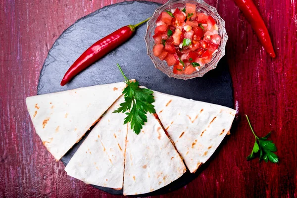 Mexican quesadilla kırmızı ahşap arka plan üzerinde siyah arduvaz taş plaka üzerinde salsa ile. Biber biber. Üstten Görünüm.