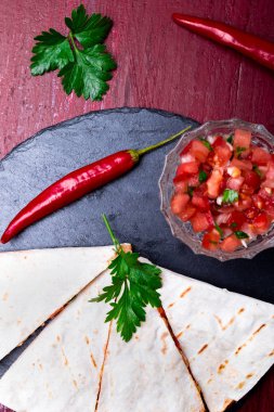 Mexican quesadilla kırmızı ahşap arka plan üzerinde siyah arduvaz taş plaka üzerinde salsa ile. Biber biber. Üstten Görünüm.