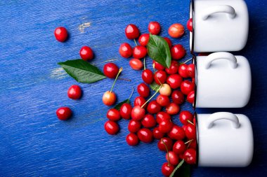 Dağınık kiraz emaye bardak dan. Kiraz demir Kupası mavi ahşap zemin üzerinde. Sağlıklı, yaz meyve. Kiraz. Üç. Üstten Görünüm.