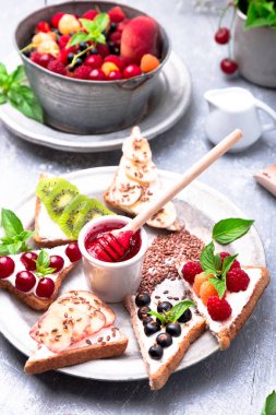 Gri arka plan üzerinde meyve tost. Sağlıklı kahvaltı. Temiz yemek. Diyet kavramı. Tahıl ekmek dilimleri ile krem peynir ve çeşitli meyve, meyveler, tohumlar. Vejetaryen.