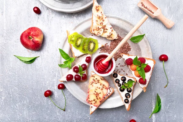 Tostadas de fruta sobre fondo gris. Desayuno saludable. Comer limpio. Concepto de dieta. Rebanadas de pan de grano con queso crema y varias frutas, bayas, semillas. Vegetariano. Vista superior . —  Fotos de Stock