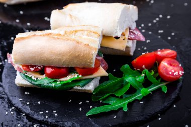 Jamon, roka, domates, peynir taş kayrak siyah arka plan üzerine ile sandviç. Yakın çekim