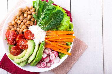 Vegan Buda kase Beyaz ahşap zemin üzerinde. Havuç, marul, kiraz domates, turp, avokado ve Nohut ile top. Vejetaryen, sağlıklı, detoks gıda kavramı. Üstten Görünüm.