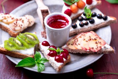 Kırmızı zemin üzerine meyve tost. Sağlıklı kahvaltı. Temiz yemek. Diyet kavramı. Tahıl ekmek dilimleri ile krem peynir ve çeşitli meyve, meyveler, tohumlar. Vejetaryen.