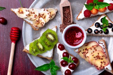 Kırmızı zemin üzerine meyve tost. Sağlıklı kahvaltı. Temiz yemek. Diyet kavramı. Tahıl ekmek dilimleri ile krem peynir ve çeşitli meyve, meyveler, tohumlar. Vejetaryen. Üstten Görünüm.