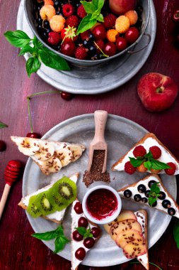 Kırmızı zemin üzerine meyve tost. Sağlıklı kahvaltı. Temiz yemek. Diyet kavramı. Tahıl ekmek dilimleri ile krem peynir ve çeşitli meyve, meyveler, tohumlar. Vejetaryen. Üstten Görünüm.