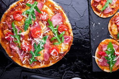 Ev yapımı pizza salam, domates, roka siyah arduvaz gemide. Üstten Görünüm.