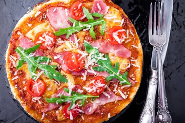 Ev yapımı pizza salam, domates, roka siyah arduvaz gemide. Üstten Görünüm.