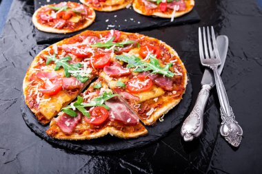 Ev yapımı pizza salam, domates, roka siyah arduvaz gemide. Yakın çekim.