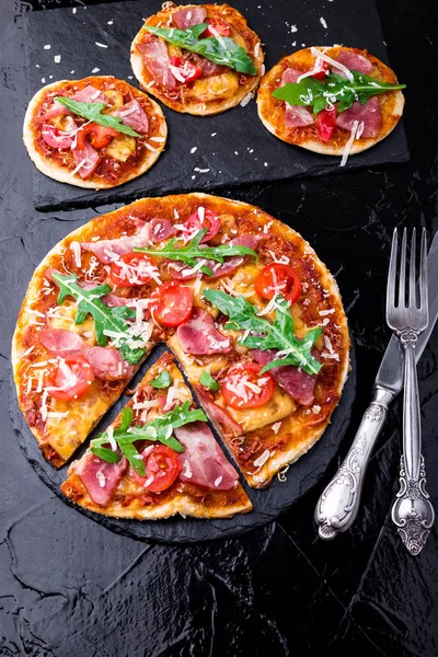 Ev yapımı pizza salam, domates, roka siyah arduvaz gemide. Üstten Görünüm.