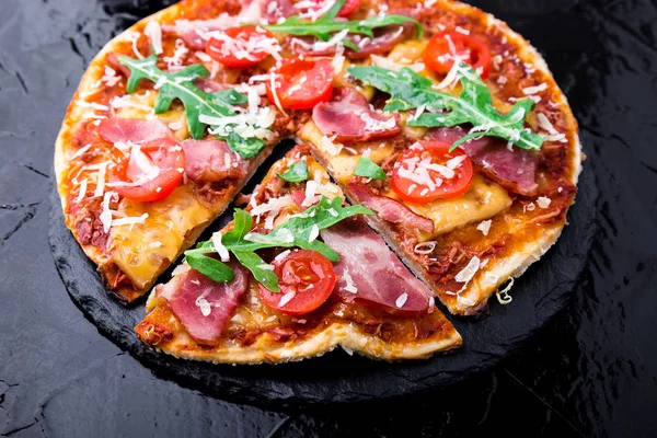 Ev yapımı pizza salam, domates, roka siyah arduvaz gemide. Yakın çekim.