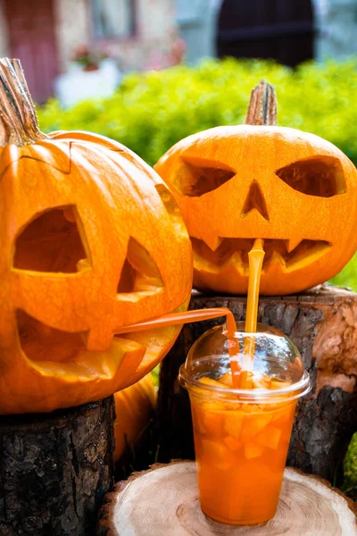 Arka planda balkabağı desenli Cadılar Bayramı kokteyli. Parti için yumruk. İki Jack-o-Lantern kokteyl içiyor..