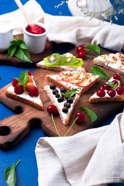 Ahşap rustik arka plan mavi tahtada meyve tost. Sağlıklı kahvaltı. Temiz yemek. Diyet kavramı. Tahıl ekmek dilimleri ile krem peynir ve çeşitli meyve, meyveler, tohumlar. Vejetaryen.