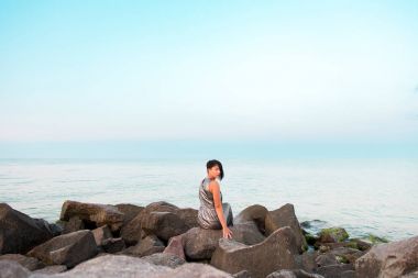 Kadın parlak gümüş elbisenin içinde taş deniz sahilde oturuyor.