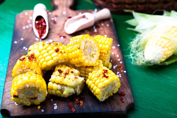 Tranches de maïs grillées sur une planche de bois avec sel et poivre rouge séché. Gros plan . — Photo