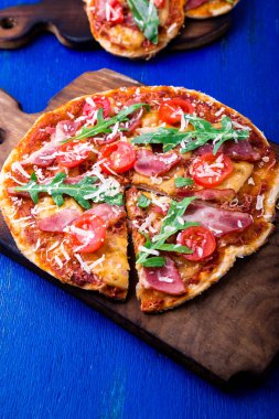 Ev yapımı pizza salam, domates, roka ahşap Pano mavi zemin üzerine. Üstten Görünüm.