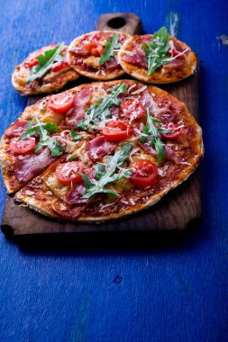 Ev yapımı pizza salam, domates, roka ahşap Pano mavi zemin üzerine.