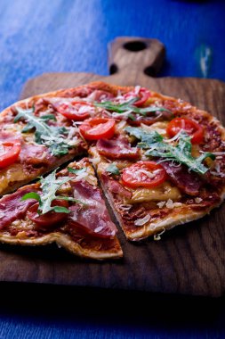 Ev yapımı pizza salam, domates, roka ahşap Pano mavi zemin üzerine.