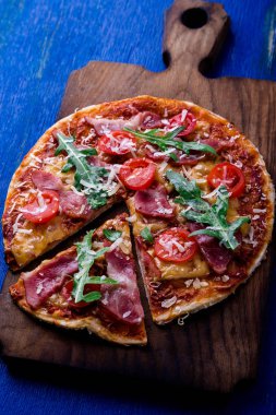 Ev yapımı pizza salam, domates, roka ahşap Pano mavi zemin üzerine.