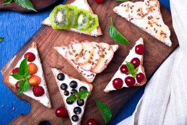 Ahşap rustik arka plan mavi tahtada meyve tost. Sağlıklı kahvaltı. Temiz yemek. Diyet kavramı. Tahıl ekmek dilimleri ile krem peynir ve çeşitli meyve, meyveler, tohumlar. Vejetaryen. Üstten Görünüm.