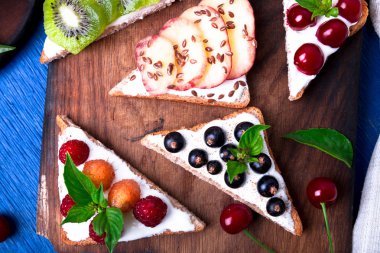 Ahşap rustik arka plan mavi tahtada meyve tost. Sağlıklı kahvaltı. Temiz yemek. Diyet kavramı. Tahıl ekmek dilimleri ile krem peynir ve çeşitli meyve, meyveler, tohumlar. Vejetaryen. Üstten Görünüm.