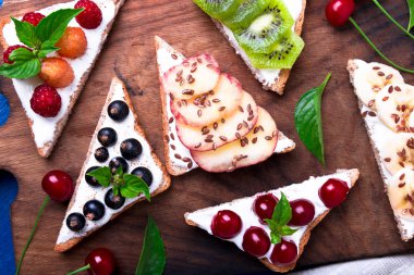 Ahşap rustik arka plan mavi tahtada meyve tost. Sağlıklı kahvaltı. Temiz yemek. Diyet kavramı. Tahıl ekmek dilimleri ile krem peynir ve çeşitli meyve, meyveler, tohumlar. Vejetaryen. Üstten Görünüm.