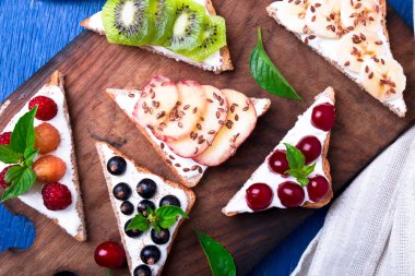 Ahşap rustik arka plan mavi tahtada meyve tost. Sağlıklı kahvaltı. Temiz yemek. Diyet kavramı. Tahıl ekmek dilimleri ile krem peynir ve çeşitli meyve, meyveler, tohumlar. Vejetaryen. Üstten Görünüm.