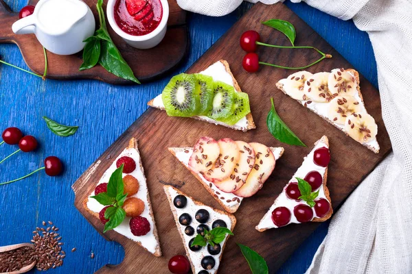 Ahşap rustik arka plan mavi tahtada meyve tost. Sağlıklı kahvaltı. Temiz yemek. Diyet kavramı. Tahıl ekmek dilimleri ile krem peynir ve çeşitli meyve, meyveler, tohumlar. Vejetaryen. Üstten Görünüm.