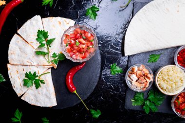 Mexican quesadilla ve siyah arduvaz taş plaka üzerinde salsa malzemelerle. Üstten Görünüm