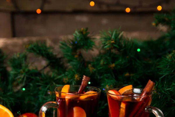 Χριστουγεννιάτικο ζεστό κρασί με φρούτα και μπαχαρικά σε ξύλινο τραπέζι. Χριστούγεννα διακοσμήσεις στο παρασκήνιο. Δύο ποτήρια. Χώρο αντίγραφο. — Φωτογραφία Αρχείου